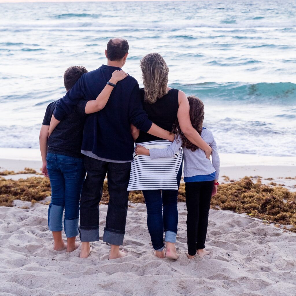 family hugging on the sand looking out to the sea