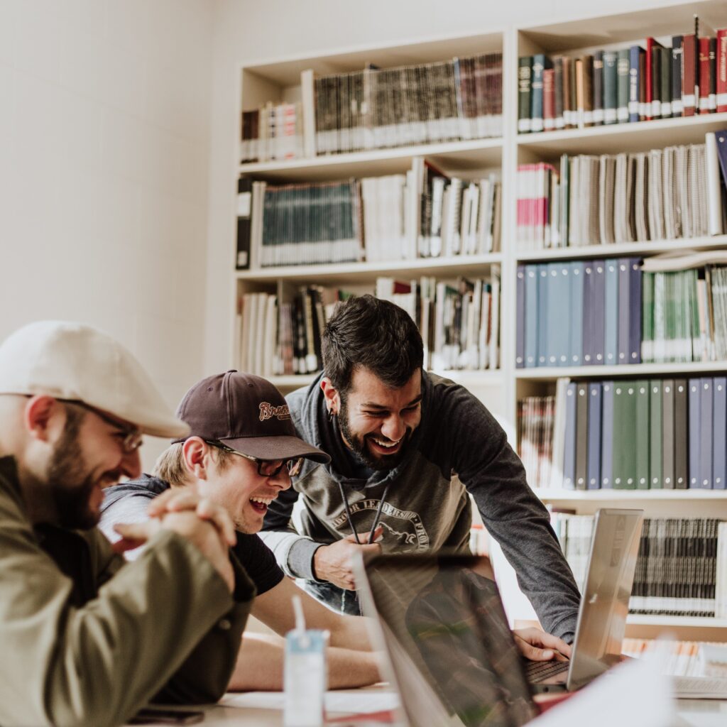 3 men gathered around a laptop in a library