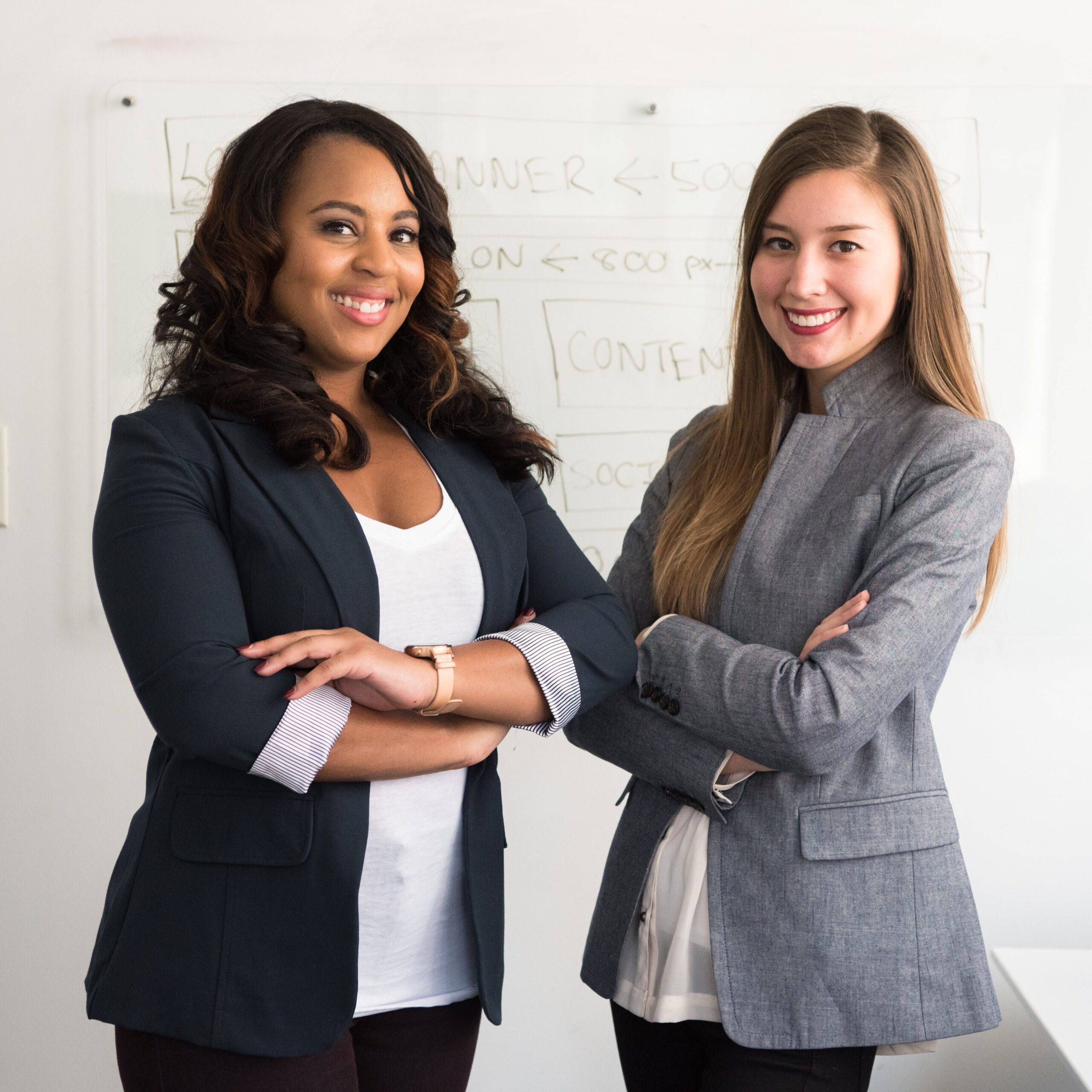 two women in suits with their arms folded smiling