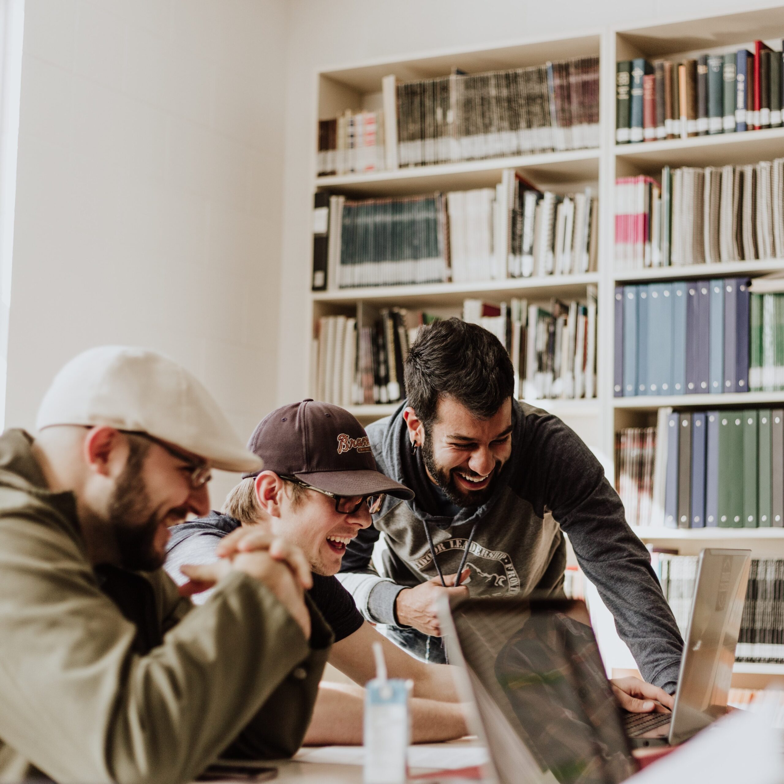 3 men gathered around a laptop in a library